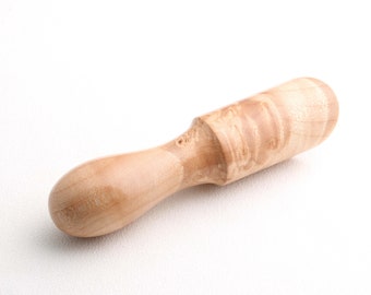 May include: A light-colored wooden muddler with a rounded handle and a cylindrical head. The wood grain is visible, and the muddler is designed for mixing ingredients in cocktails or other beverages. The handle is smooth and comfortable to hold.
