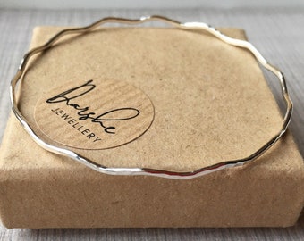 May include: A silver bangle bracelet with a hammered texture, resting on a brown box with the text "Barsha Jewellery".