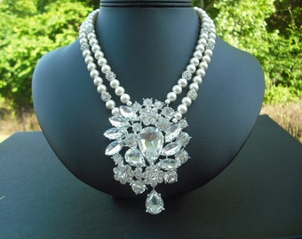 Op de afbeelding: Een zilveren ketting met een grote, heldere strass-hanger en een dubbele rij nepparels.