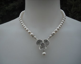 Op de afbeelding: Een witte parelketting met een zilveren hanger met een cluster van heldere strass.