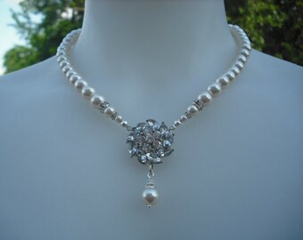 Op de afbeelding: Een witte parelketting met een zilveren hanger met een cluster van heldere strass steentjes. De hanger heeft een enkele parel druppel.