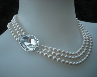 May include: A three-strand pearl necklace with a large, clear crystal pendant.