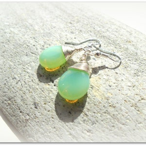 May include: A pair of silver earrings with green and yellow teardrop-shaped glass beads wrapped in silver wire.