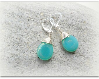 May include: A pair of silver dangle earrings with light blue teardrop-shaped stones. The stones are wrapped in silver wire.