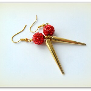 May include: A pair of gold earrings with red rhinestone balls and gold spike accents.