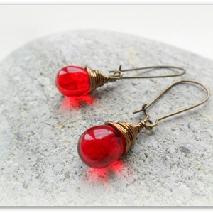 May include: A pair of red glass bead earrings with brass wire wrapped around the beads and brass wire hooks.