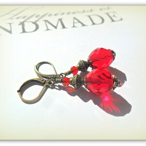 May include: Red glass bead earrings with antique brass hooks and accents. The earrings are on a white surface with the text "Happiness is Handmade" visible in the background.