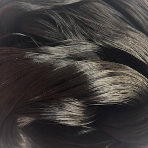 Könnte beinhalten: Nahaufnahme eines Bündels dunkelbraunen menschlichen Haars. Das Haar ist lang und glatt, mit einem leichten Glanz. Die Haarspitzen sind leicht ausgefranst.