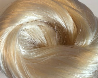 May include: A close-up of a bundle of soft, white, silky fibers. The fibers are tightly packed together and have a smooth, shiny texture.