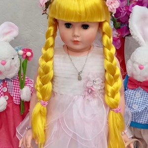 May include: A yellow haired doll wearing a white dress with pink ruffles and a flower crown. The doll has blue eyes and is holding a basket. The doll is standing next to a white bunny with a pink bow.