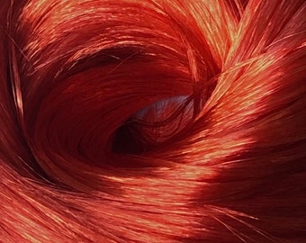 May include: Close-up of vibrant, reddish-orange hair strands. The hair is arranged in a swirling pattern, with light reflecting off the strands, creating highlights and shadows. The overall effect is a dynamic, textured look.