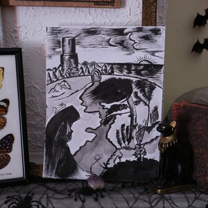 Peut inclure: Une présentation encadrée de papillons, un dessin à l'encre noir et blanc d'un paysage, une figurine de chat noir et un livre décoratif. Les papillons sont jaunes, oranges et bruns. Le dessin représente une tour et une figure.