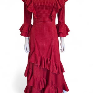May include: A red, floor-length dress with a polka dot pattern. The dress features ruffled sleeves and a tiered skirt. The dress is displayed on a mannequin against a white background. The dress has a boat neckline.