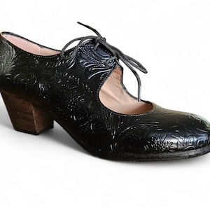 Puede incluir: Zapato de cuero negro con dise&ntilde;o floral en relieve. El zapato tiene un tac&oacute;n de madera y cierre de cordones. El tac&oacute;n mide aproximadamente 6,35 cm.