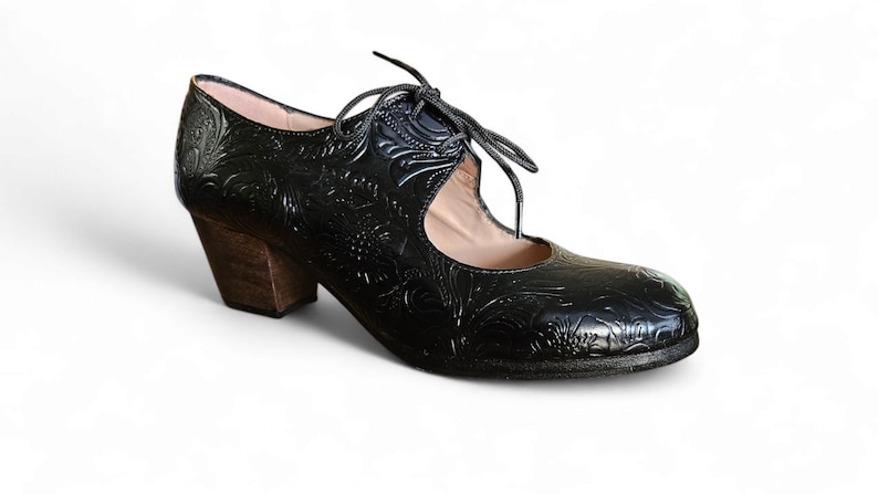 Puede incluir: Zapato de cuero negro con dise&ntilde;o floral en relieve. El zapato tiene un tac&oacute;n de madera y cierre de cordones. El tac&oacute;n mide aproximadamente 6,35 cm.