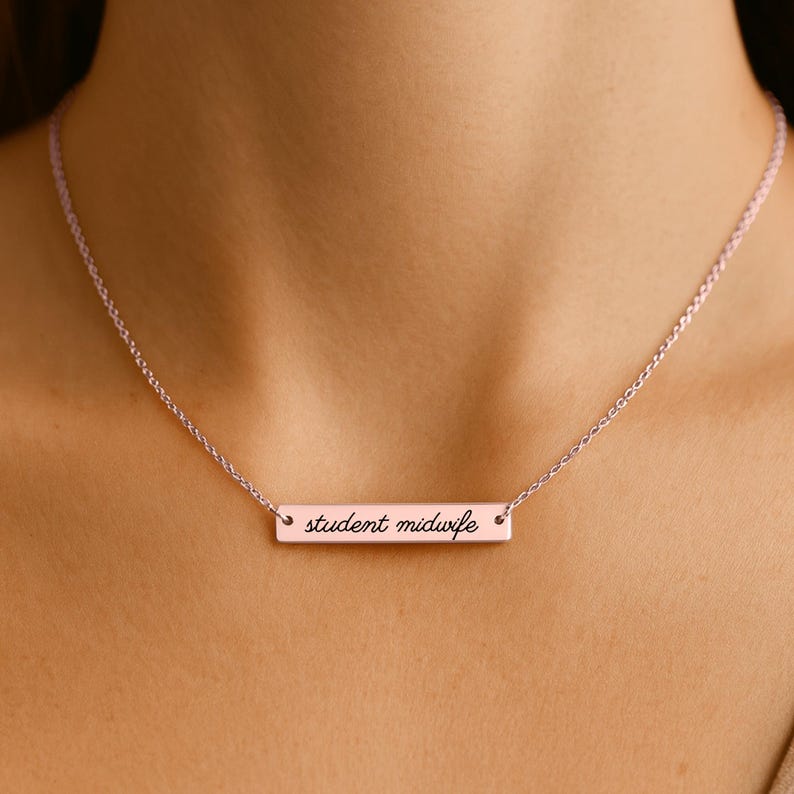 May include: A rose gold-toned bar necklace featuring a delicate chain and a horizontal rectangular pendant. The pendant is engraved with the text student midwife in a black cursive script font, centered on the polished metal surface.