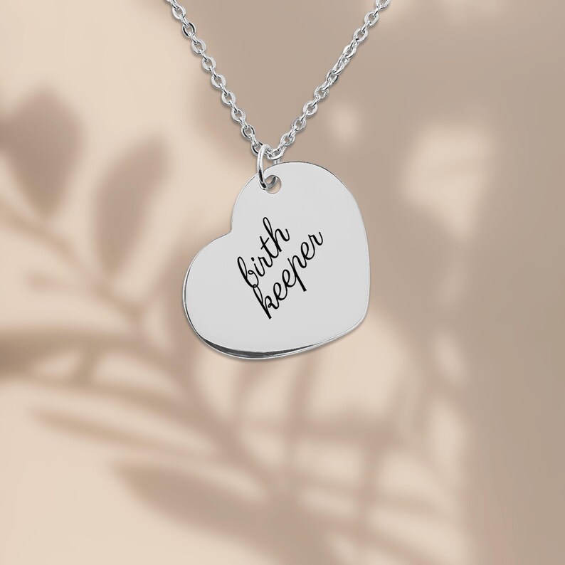 Pu&ograve; includere: Una collana con ciondolo a forma di cuore color argento con il testo birth keeper inciso in un carattere corsivo nero. Il ciondolo &egrave; appeso a una delicata catenina color argento, creando un gioiello semplice e raffinato.