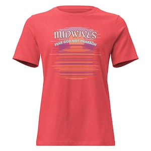 Pode incluir: Uma t-shirt vermelha de manga curta com um gráfico de um pôr do sol com linhas horizontais em tons de laranja, roxo e amarelo. O texto MIDWIVES está impresso a branco sobre o texto FEAR GOD NOT PHARAOH em azul claro.