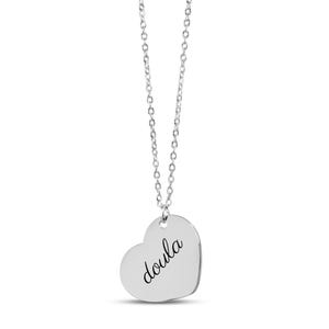 Puede incluir: Un collar con colgante en forma de coraz&oacute;n plateado que presenta la palabra doula grabada en una tipograf&iacute;a cursiva negra. El colgante cuelga de una delicada cadena plateada con peque&ntilde;os eslabones ovalados, creando una joya sencilla.