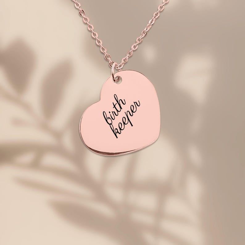 Pu&ograve; includere: Una collana con ciondolo a forma di cuore in oro rosa con il testo inciso birth keeper in un carattere corsivo nero. Il ciondolo &egrave; appeso a una catenina abbinata in oro rosa e presenta una superficie metallica liscia e lucida.
