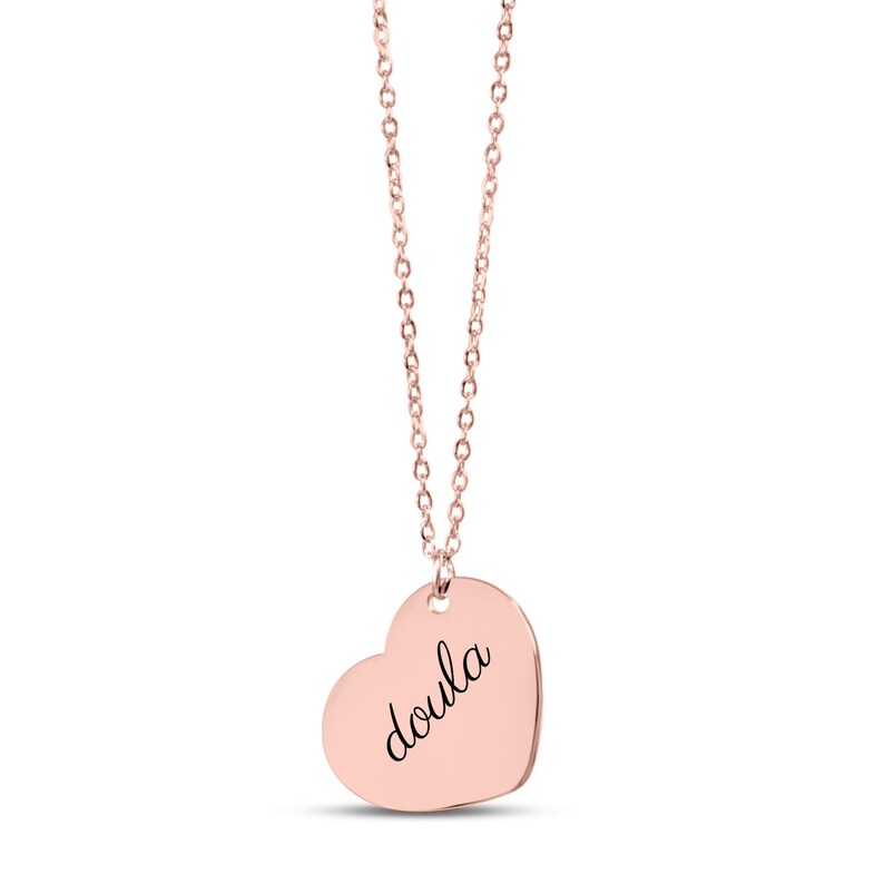 Puede incluir: Un collar con colgante en forma de coraz&oacute;n de color oro rosa que presenta la palabra doula grabada en una tipograf&iacute;a cursiva negra. El colgante cuelga de una delicada cadena a juego de color oro rosa con peque&ntilde;os eslabones ovalados, creando una joya sencilla.