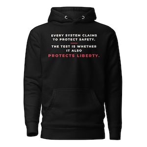 Puede incluir: Una sudadera con capucha negra con texto en blanco que dice: EVERY SYSTEM CLAIMS TO PROTECT SAFETY. THE TEST IS WHETHER IT ALSO PROTECTS LIBERTY. La palabra LIBERTY está impresa en rojo y una línea horizontal roja separa el texto.