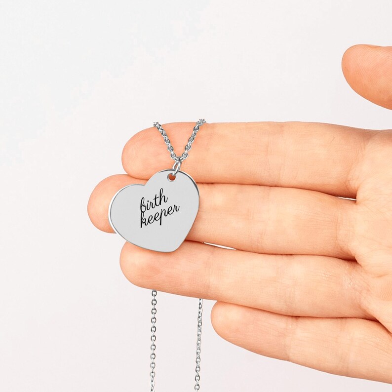 Pu&ograve; includere: Una collana con ciondolo a forma di cuore color argento che riporta l'incisione birth keeper in un carattere corsivo nero. Il ciondolo &egrave; fissato a una sottile catenina in metallo color argento con piccoli anelli circolari.