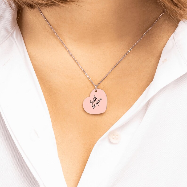 Pu&ograve; includere: Una collana a catena color argento con un ciondolo a forma di cuore con finitura rosa chiaro. Il ciondolo &egrave; inciso con il testo nero "birth keeper" in un carattere corsivo, centrato sulla superficie liscia del cuore.