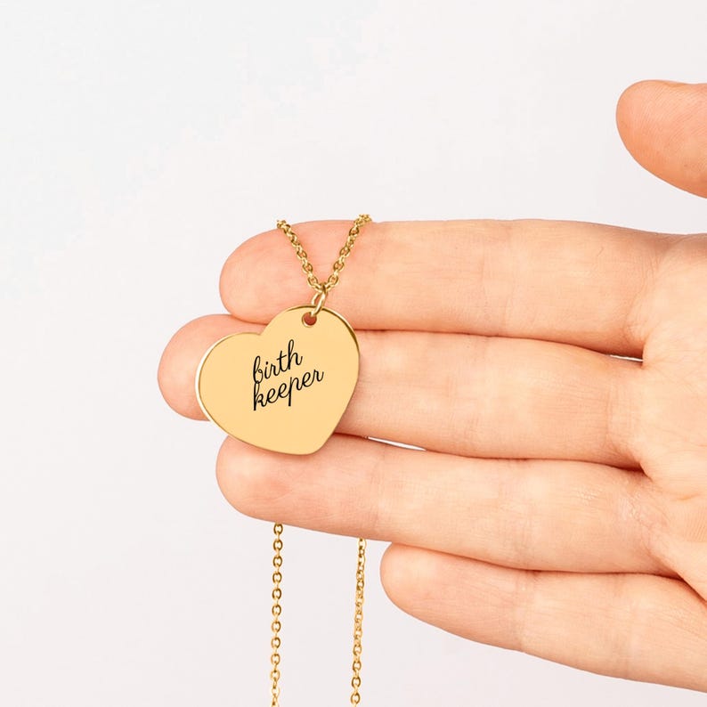 Pu&ograve; includere: Una collana con ciondolo a forma di cuore color oro con il testo nero inciso "birth keeper" in carattere corsivo. Il ciondolo &egrave; sospeso a una delicata catenina color oro, caratterizzata da una finitura metallica liscia e lucida.