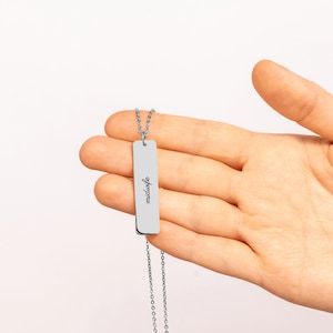 May include: A silver-toned vertical bar pendant necklace featuring the word midwife engraved in a black script font. The rectangular metal charm hangs from a delicate matching chain, showcasing a clean and polished metallic finish.