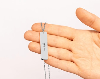 May include: A silver-toned vertical bar pendant necklace featuring the word midwife engraved in a black script font. The rectangular metal charm hangs from a delicate matching chain, showcasing a clean and polished metallic finish.