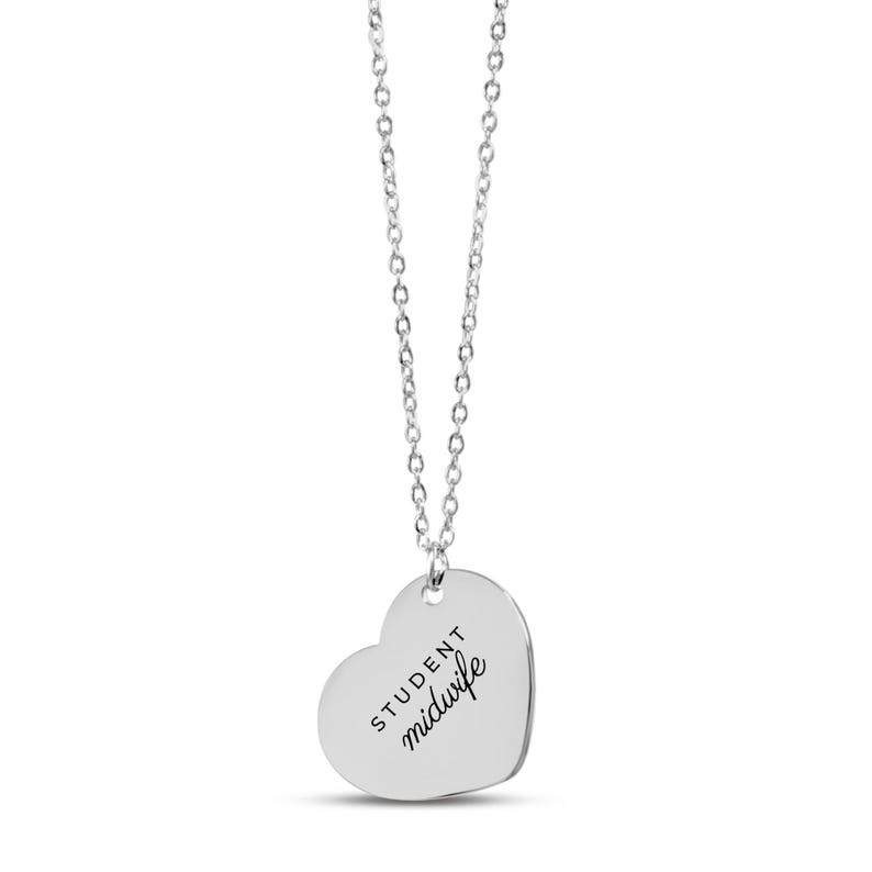 May include: A silver-toned heart-shaped pendant necklace featuring a delicate chain and a smooth metal charm. The pendant is engraved with the text "STUDENT midwife" in a combination of block and script lettering centered on the surface.