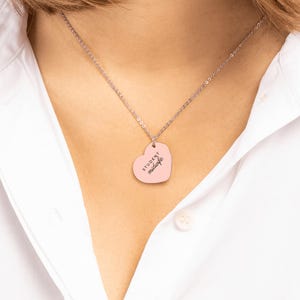May include: A silver-toned chain necklace featuring a light pink heart-shaped pendant. The pendant is engraved with the black text "STUDENT midwife" in a combination of block and script lettering, centered on the smooth surface.
