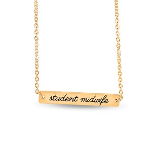 May include: A gold-toned bar necklace featuring a delicate chain and a horizontal rectangular pendant. The pendant is engraved with the text student midwife in a black cursive script font, centered on the polished metal surface.
