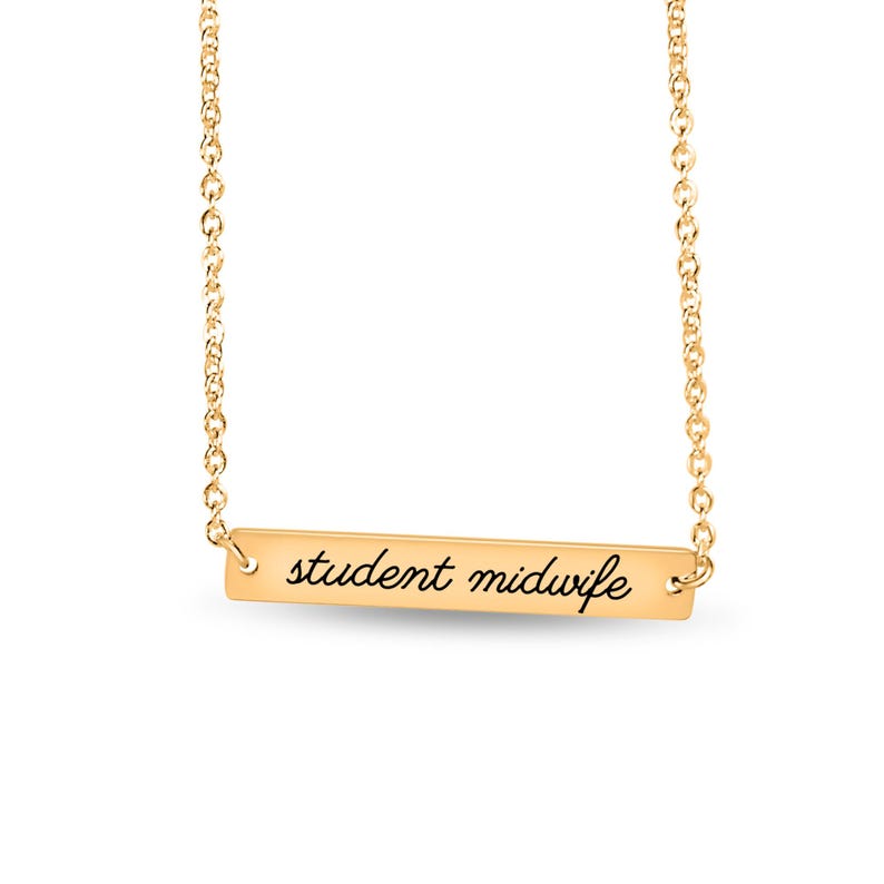 May include: A gold-toned bar necklace featuring a delicate chain and a horizontal rectangular pendant. The pendant is engraved with the text student midwife in a black cursive script font, centered on the polished metal surface.