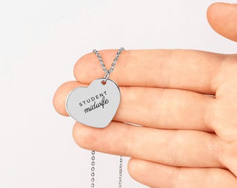 May include: A silver-toned heart-shaped pendant necklace featuring the engraved text "STUDENT midwife" in a combination of block and script lettering. The pendant hangs from a delicate silver-toned chain link necklace.