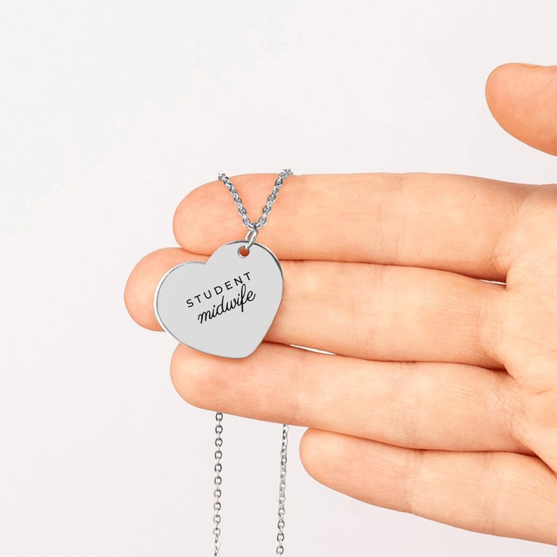 May include: A silver-toned heart-shaped pendant necklace featuring the engraved text "STUDENT midwife" in a combination of block and script lettering. The pendant hangs from a delicate silver-toned chain link necklace.