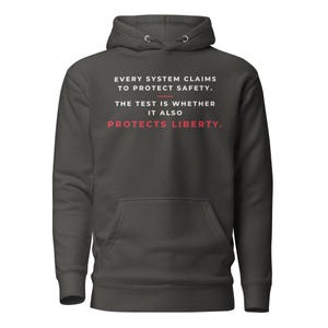 Puede incluir: Una sudadera con capucha de color gris carbón que incluye un bolsillo tipo canguro y texto en blanco: EVERY SYSTEM CLAIMS TO PROTECT SAFETY. THE TEST IS WHETHER IT ALSO PROTECTS LIBERTY. La palabra LIBERTY está impresa en rojo.