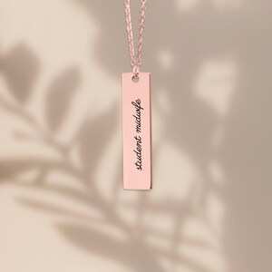 Puede incluir: Un collar con colgante de barra vertical en oro rosa que presenta el texto grabado student midwife en una fuente cursiva negra. El colgante cuelga de una cadena a juego en oro rosa, creando una pieza de joyer&iacute;a sencilla.