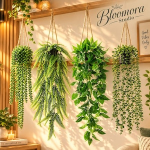May include: Four artificial hanging plants in black pots suspended by rope. The plants include a string of pearls, a fern, a leafy vine, and a trailing succulent. The text Bloomora Studio and Good Vibes Only is visible in the background.