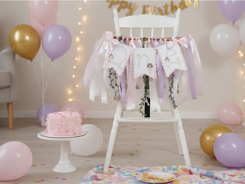 May include: A white high chair decorated with a banner that spells "one" with illustrations of fairies. The chair is adorned with pink, white, and lavender ribbons. A pink cake sits on a white cake stand, surrounded by balloons in gold, pink, and lavender.