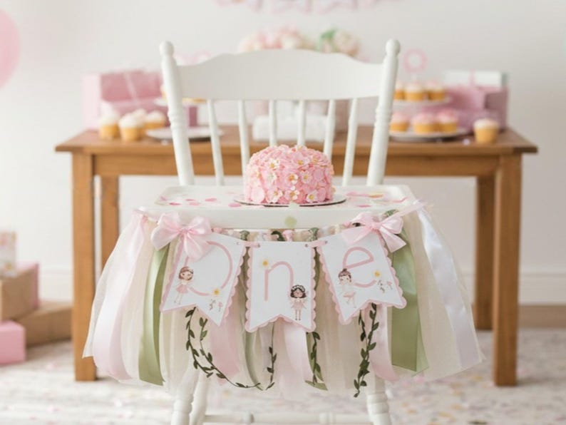 May include: A white high chair decorated for a first birthday. The chair has a pink and white tutu skirt with bows and a banner that says "one". A small pink cake sits on the tray. Cupcakes and a table are in the background.