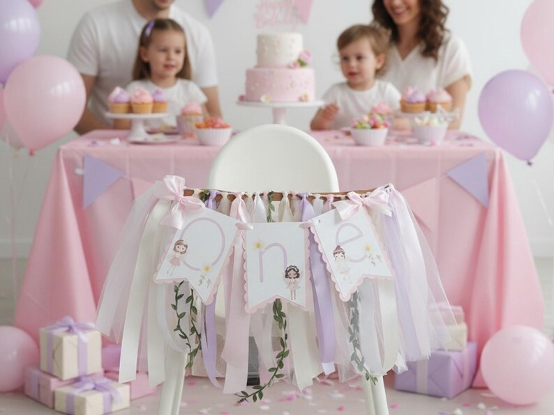 May include: A high chair decorated with a banner that says "One" with a ballerina design. The banner is decorated with ribbons in shades of pink, white, and lavender. A pink tablecloth, balloons, and a cake are in the background.