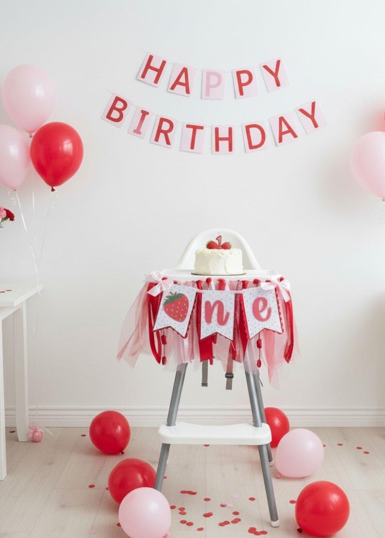 May include: A white high chair decorated with a red and white tulle skirt and a banner featuring a strawberry and the word one. A small white cake with a number one topper sits on the tray. A Happy Birthday banner hangs on the wall above.