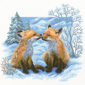 May include: Two red foxes with white markings are snuggled together in a snowy winter scene. The foxes are looking at each other with their noses touching. The background features a blue sky, snow-covered hills, and a pine tree.