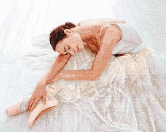 Pode incluir: Uma bailarina com um tutu branco e sapatilhas de ponta está deitada sobre uma superfície branca. Ela está encolhida com a cabeça apoiada no braço. A luz é suave e etérea, criando uma atmosfera de sonho.