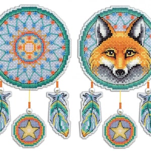 Peut inclure: Deux attrape-rêves avec des motifs géométriques bleus, verts, oranges et jaunes. Un attrape-rêves représente un visage de renard, l'autre un motif circulaire. Les deux attrape-rêves ont des plumes et des étoiles qui pendent.