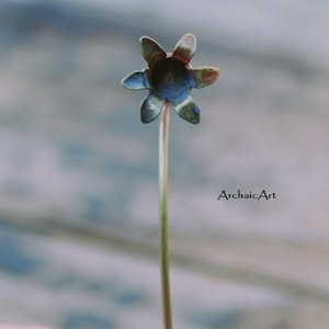 May include: A gold metal flower pin with a dark blue centre and five petals. The pin is held in a hand.