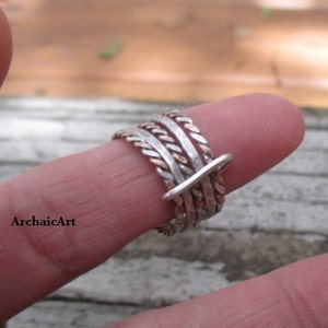 May include: A silver and copper ring with a braided design. The ring is worn on a finger.