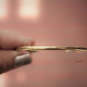 May include: A gold-toned bangle bracelet with a simple geometric design. The bracelet is engraved with a small circle on the top.
